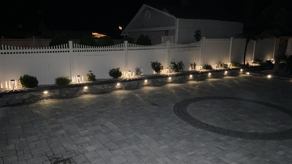 Completed paver courtyard with landscape lighting and white privacy fence by RMR & Brothers